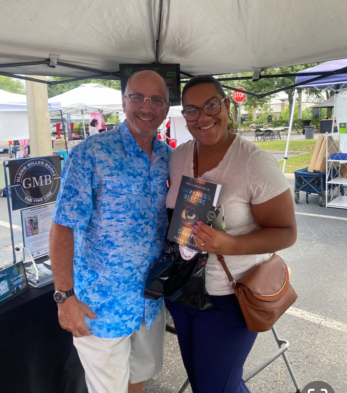 Glenn Miller with a reader holding Darkness Before Dawn at a market booth